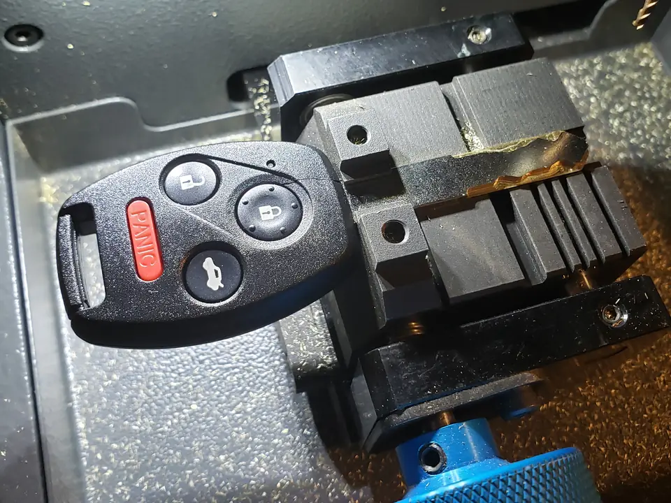 A car key fob clamped in a key machine next to a blue clamp knob