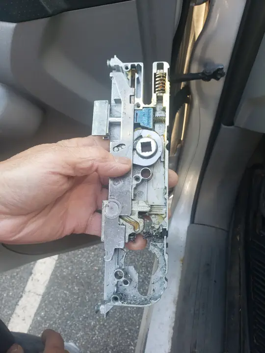 A mortise lock body held in a hand after being removed from a door