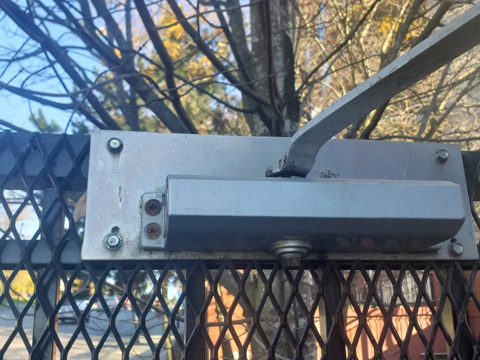 Door closer mounted on a black steel mesh security gate