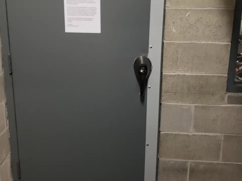 Grey steel door with a lever lock set into a brick wall beside a mailroom