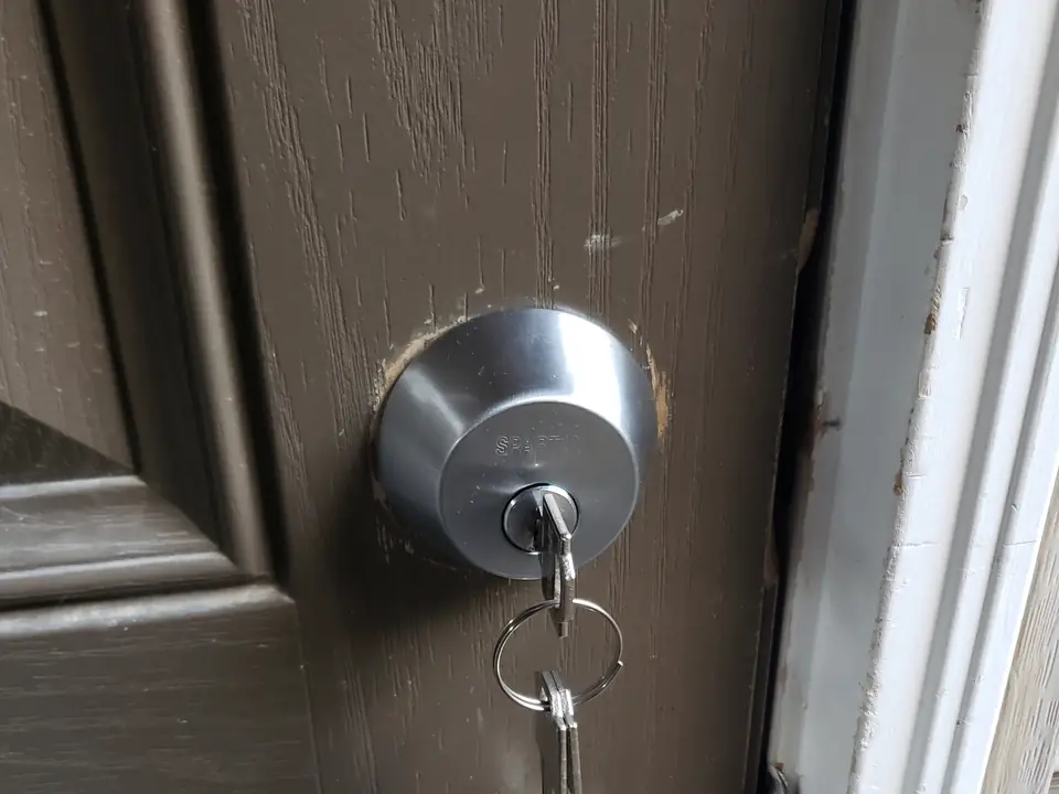 A deadbolt and lever handle on a wood-grain door with a set of keys in the lock