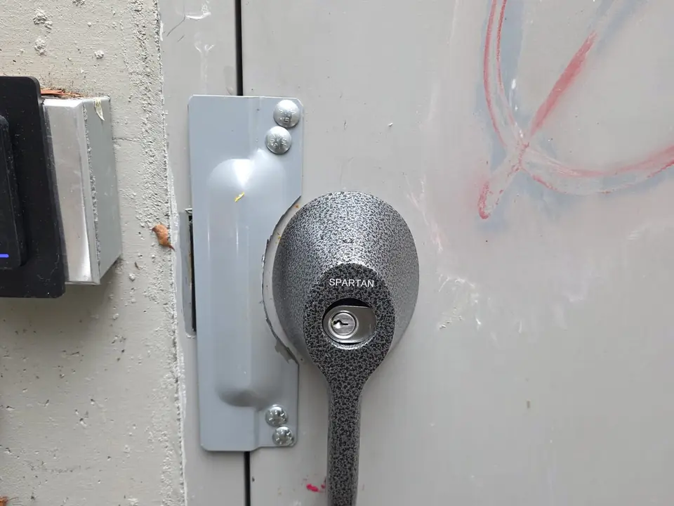 Heavy-duty cylinder lock and strike plate on a grey steel door