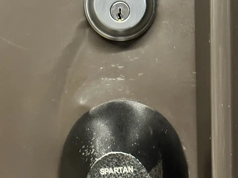 A deadbolt with a bent cover plate on a brown door
