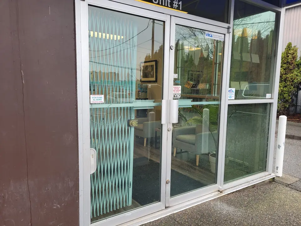 Glass storefront entrance with double doors and a metal security gate behind the glass