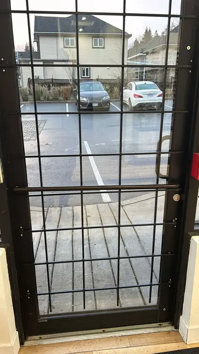 Black steel security gate with a lock, facing a parking lot
