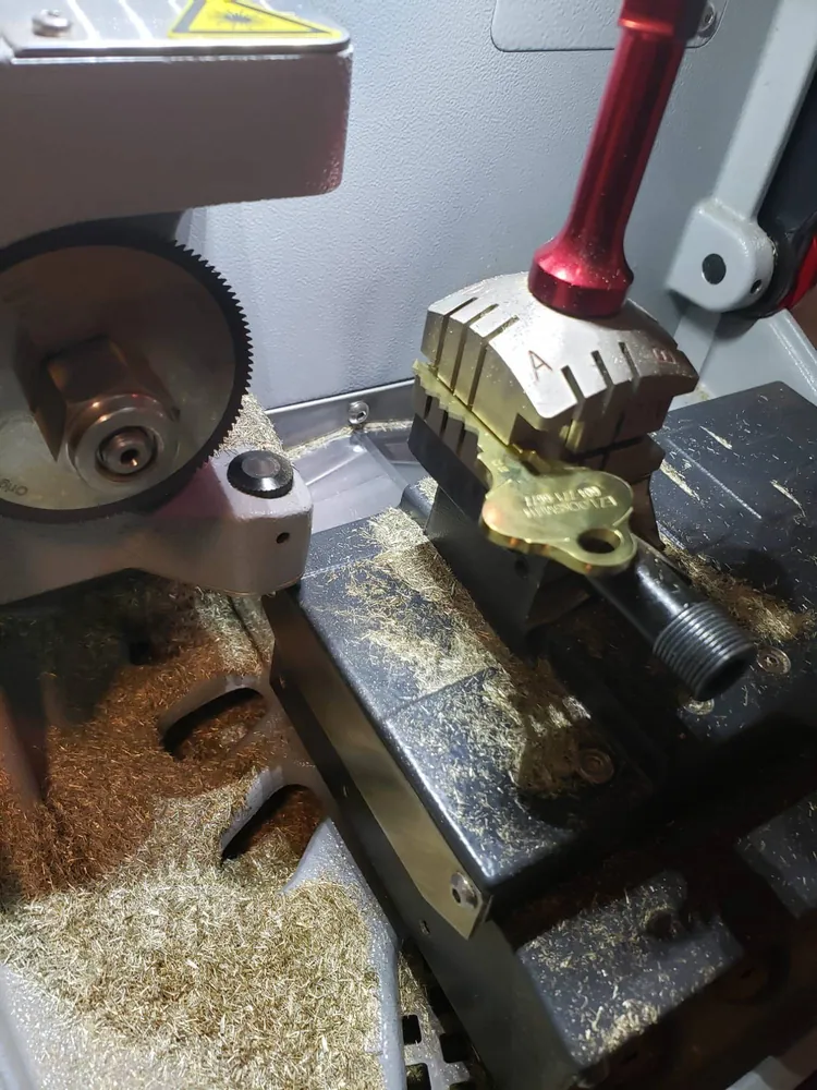 A brass key being cut on a key cutting machine, stamped with the EZ Locksmith name and phone number